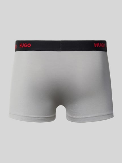 Männermodel trägt Trunk aus Baumwoll-Mix im 3er-Pack von HUGO in Grau mit schwarzem Bund und rotem Logo, Ganzkörperansicht Rückansicht. Herren TRUNK.