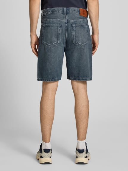 Männermodel trägt Loose Fit Jeansshorts aus reiner Baumwolle von Calvin Klein Jeans in Denim-Optik mit Label-Patch, 5-Pocket-Design, Ganzkörperansicht Rückansicht.