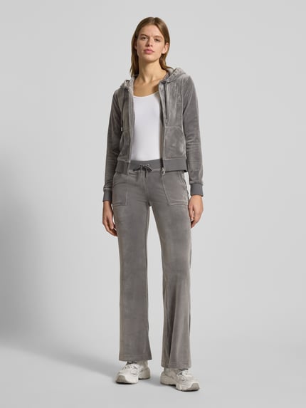 Frauenmodel trägt Low Rise Sweatpants mit elastischem Bund Modell 'LAYLA' von Juicy Couture aus grauem Baumwoll-Mix mit Stretch-Anteil, Flared-Cut, Eingrifftaschen, Ganzkörperansicht von vorne.