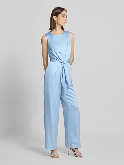 Frauenmodel trägt Jumpsuit aus Satin mit Bindegürtel von Christian Berg Cocktail in Hellblau, gerades Bein, leicht tailliert, Ganzkörperansicht von vorne.