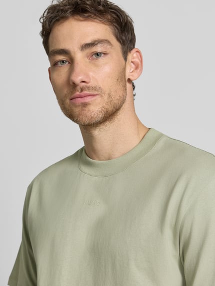 Mężczyzna nosi Regular Fit T-Shirt aus reiner Baumwolle Modell 'DAPOLINO' von HUGO w kolorze jednolitym, okrągły dekolt, krótki rękaw, napis z logo, jersey, przód, zbliżenie na górną część ciała.