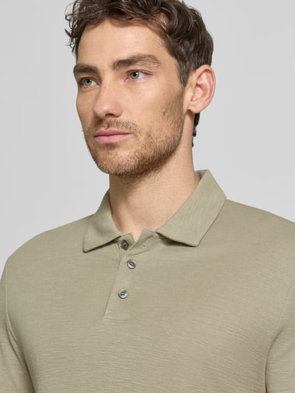 Męski model nosi Slim Fit Poloshirt aus Lyocell-Leinen-Mix Modell 'DULINEN' od HUGO, jednobarwny, krój slim fit, z kołnierzykiem polo, krótki rękaw, label-aplikacja, krótka listwa guzikowa, materiał Lyocell-Len, zbliżenie na górną część ciała.