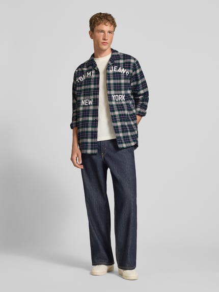 Männermodel trägt Relaxed Fit Freizeithemd aus reiner Baumwolle von Tommy Jeans in Dunkelblau-Grün kariert, helles Shirt, Jeans, Ganzkörperansicht von vorne, Herren Freizeithemd von Tommy Jeans.