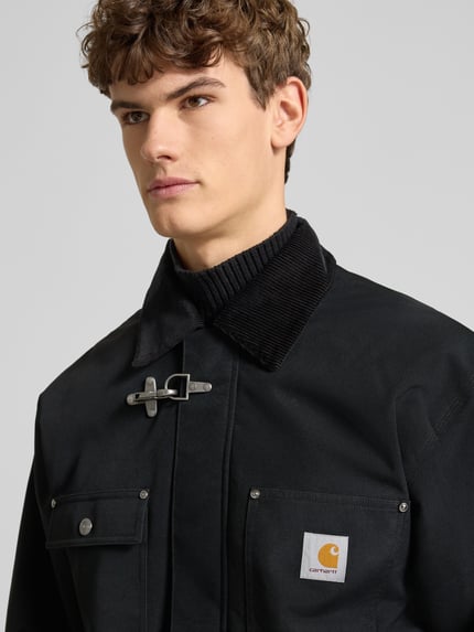 Männermodel trägt Oversized Jacke mit Logo-Patch Modell 'Adair' von Carhartt Work In Progress, schwarz, Cord-Besatz, Nahaufnahme Oberkörper.