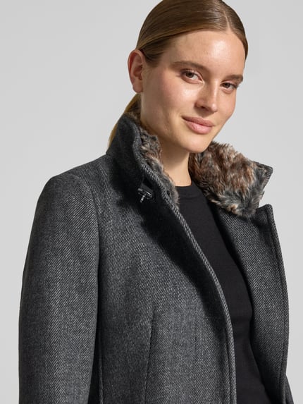 Frauenmodel trägt Mantel mit Kunstfell und Pattentaschen von Christian Berg Woman Selection in dunklem Grau, Material-Mix, Nahaufnahme Oberkörper.