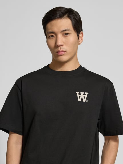 Männermodel trägt Herren T-Shirt mit Rundhalsausschnitt Modell 'Liam' von Wood Wood, Schwarz, Label-Print, Reine Baumwolle, Regular-Fit, Nahaufnahme Oberkörper.