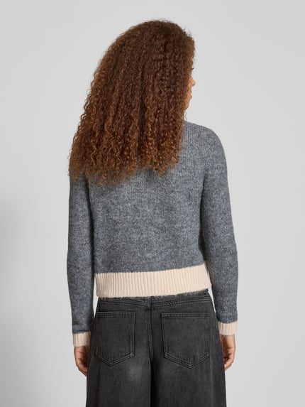 Vrouwenmodel draagt Shaped Fit Strickjacke mit Woll-Anteil Modell 'MAGGIE LIFE' van Only, meerkleurig gebreid, geribde zoom, eenrijige knopen, label stitching, v-hals, lange mouwen, detailzak, Ganzkörperansicht Rückansicht.