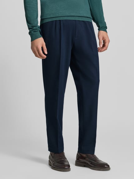Männermodel trägt Regular Fit Bundfaltenhose mit Seitenriegel von MCNEAL in Dunkelblau, glatte Textur, Nahaufnahme Oberkörper. Herren Bundfaltenhose, 1er-Bundfalte, Seitenriegel, Eingrifftaschen, Gesäßtaschen, Bundweite 45 cm, Innenbeinlänge 78 cm.