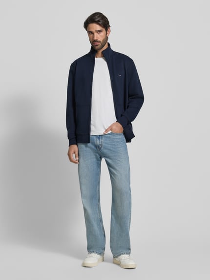 Männermodel trägt Regular Fit Sweatjacke aus Baumwoll-Mix von Tommy Hilfiger in Dunkelblau mit Label Stitching, Reißverschluss, unifarben, Ganzkörperansicht von vorne.
