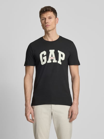 Männermodel trägt T-Shirt mit Logo und Rundhalsausschnitt von GAP in Schwarz, Reine Baumwolle, Regular-Fit, Rückenlänge 69 cm, Ganzkörperansicht von vorne.