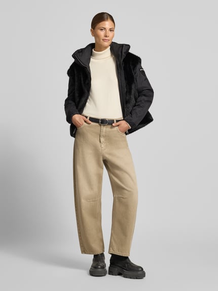 Frauenmodel trägt Regular Fit Jacke aus Kunstfell Modell 'JUNIPER' von Blauer USA in Schwarz, kombiniert mit beigem Rollkragenpullover und weiter Hose, Zweiwege-Reißverschluss, Stehkragen, Ganzkörperansicht von vorne.