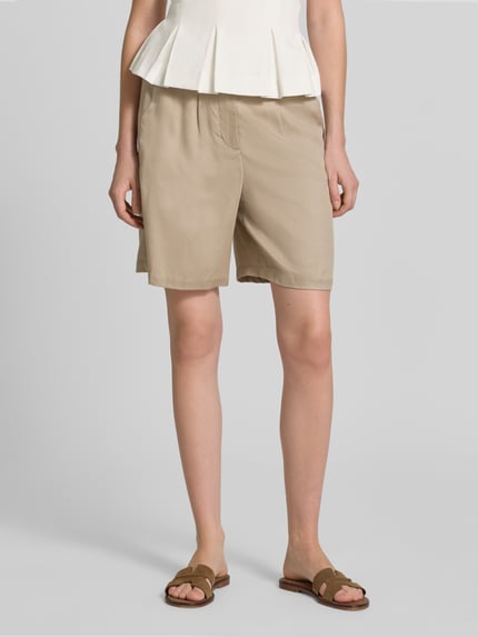 Modelka kobieca nosi Regular Fit Bermudas aus Lyocell od Tom Tailor, beżowe, gładkie, z paskiem, kieszeniami, delikatna tkanina, krój regular fit, widok z przodu, cała sylwetka.