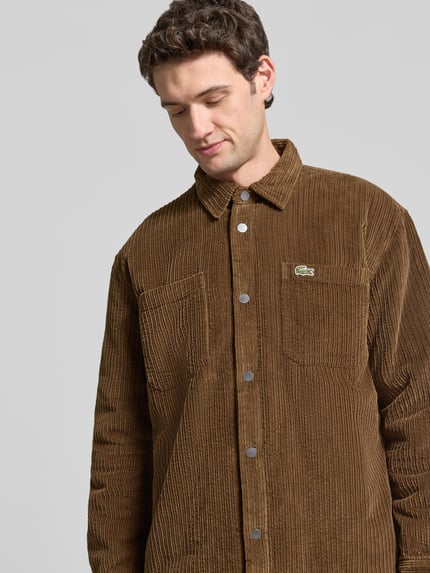 Männermodel trägt Regular Fit Cordhemd mit Logo-Patch von LACOSTE, braun, sichtbar Knopfleiste und Brusttasche, Nahaufnahme Oberkörper.