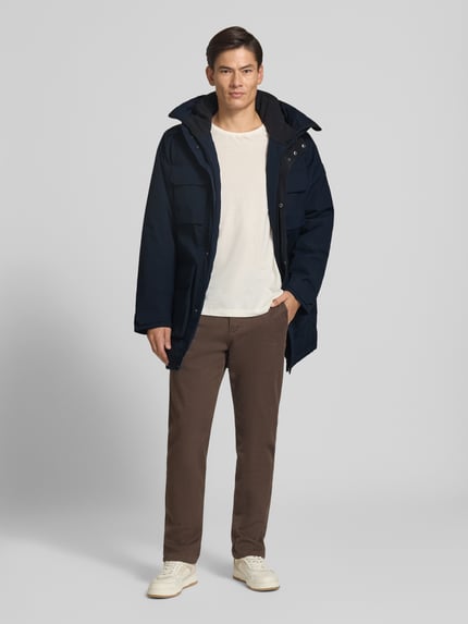 Männermodel trägt Parka mit Kapuze und Pattentaschen Modell 'AIDEN' von Didriksons in Dunkelblau, Ganzkörperansicht von vorne. Regular Fit, verdeckter Reißverschluss, Rückenlänge 95 cm, Schulterbreite 47 cm, Brustweite 55 cm, Ärmellänge 68 cm.