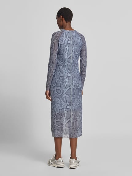 Frauenmodel trägt Midikleid mit Schlangenmuster von Marc Cain in Blau-Grau, eng anliegend, semitransparent, Rückansicht Ganzkörperansicht.