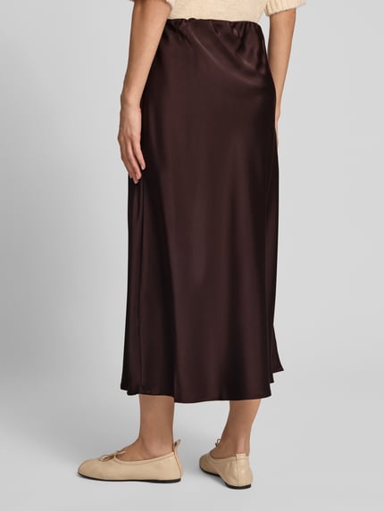 Frauenmodel trägt Midi-Rock aus Satin Modell 'Ve44rona' von ZABAIONE in Dunkelbraun, A-Linie, elastischer Bund, Ganzkörperansicht Rückansicht. Bundweite bei Größe S: 35 cm, Gesamtlänge bei Größe S: 95 cm.