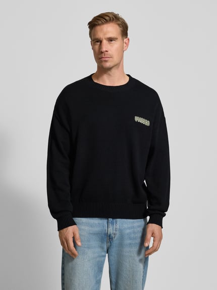 Męski model nosi czarny Strickpullover mit gerippten Abschlüssen Modell 'Kurt' od WOODBIRD z bawełnianego miksu, luźny krój, widok z przodu, całe ciało.