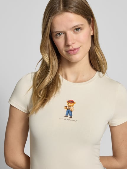 Frauenmodel trägt Slim Fit T-Shirt mit Logo-Print Modell 'Sweet' von Review in Beige, Rundhalsausschnitt, elastischer Baumwoll-Mix, Nahaufnahme Oberkörper.