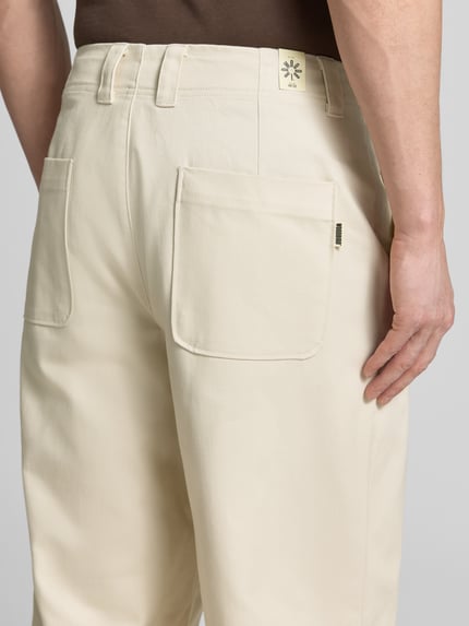 Männermodel trägt Chino mit französischen Eingrifftaschen von WOODBIRD aus reiner Baumwolle in Creme, Loose-Fit, Detailaufnahme Rückansicht.