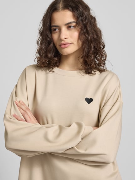 Vrouwenmodel draagt Relaxed Fit Pullover met hartborduursel model 'TALIA' van Pieces, effen, ronde hals, lange mouw, close-up bovenlichaam.