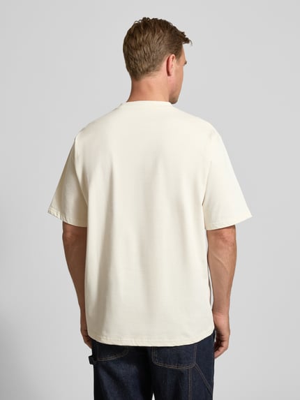 Männermodel trägt T-Shirt mit Motiv-Print Modell 'Baine' von WOODBIRD aus Bio-Baumwolle in Creme, lockerer Schnitt, Ganzkörperansicht Rückansicht.