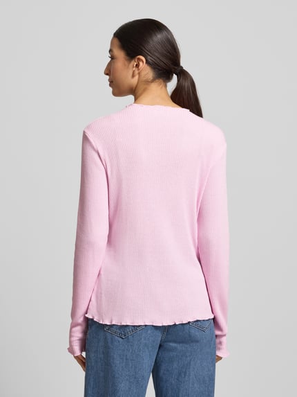 Modelka kobieta ma na sobie Slim Fit Langarmshirt mit Viskose-Anteil od s.Oliver RED LABEL w kolorze jasnoróżowym, żebrowana faktura, krój slim fit, wysoki dekolt, długie rękawy, wykończenia typu frill, label stitching; widok całej sylwetki od tyłu.