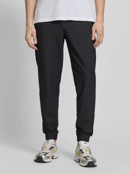 Männermodel trägt Regular Fit Sweatpants mit Strukturmuster von EA7 Emporio Armani, dunkel, elastischer Stoff, Eingrifftaschen, Nahaufnahme Unterkörper.