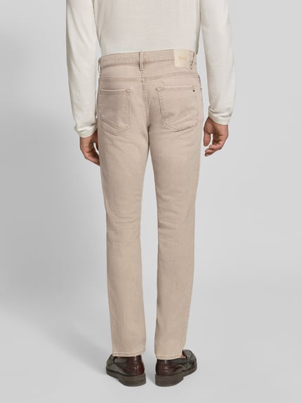 Männermodel trägt helle, beige Slim Fit Jeans aus Baumwoll-Mix Modell 'Chuck' von Brax, Herren Slim Fit Jeans, Ganzkörperansicht Rückansicht.