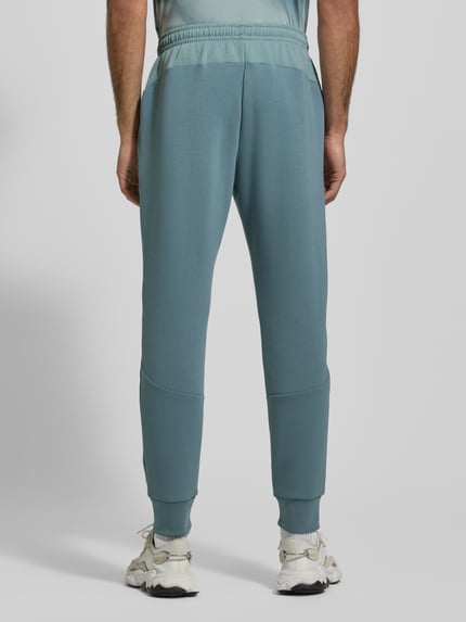 Männermodel trägt Sweatpants mit Logo Modell 'Unstoppable' von Under Armour, blau, Baumwoll-Materialmix, elastischer Bund, Ganzkörperansicht Rückansicht.