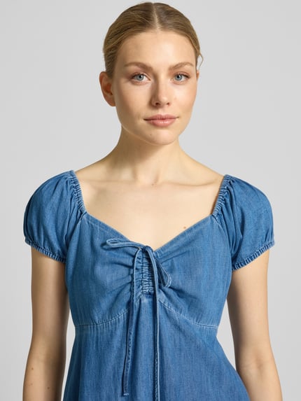 Männermodel trägt Midikleid mit Puffärmeln von GAP, dekolt w kształcie serca, marszczenia, krótkie bufiaste rękawy, wiązanie, niebieski denim, krój dopasowany, szerokość w rozmiarze S: 40 cm, długość pleców w rozmiarze S: 102 cm, długość rękawa w rozmiarze S: 12 cm, tekstura gładka, zbliżenie na górną część ciała