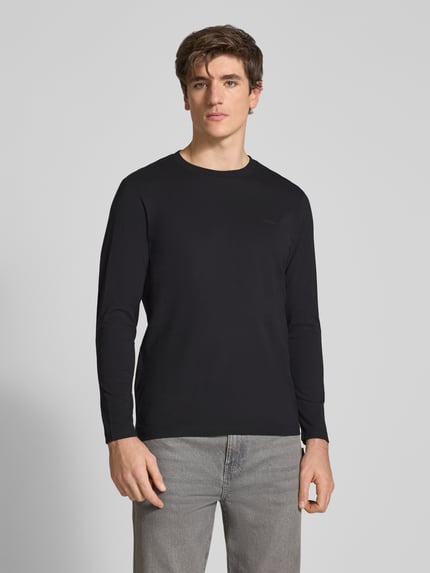 Männermodel trägt Langarmshirt mit dezentem Logo-Detail von S.OLIVER CASUAL in Schwarz, unifarben, Rundhalsausschnitt, Ganzkörperansicht von vorne.
