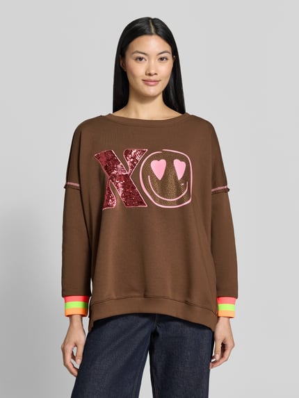 Vrouwenmodel draagt oversized sweatshirt uit puur katoen, Model 'XO Heartface' van miss goodlife, statementprint met pailletten en strass-steentjes, siernaden, ronde hals, elastische boorden, voorkant bovenlichaam close-up.