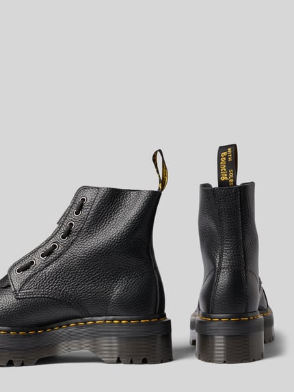 Produktfoto, schwarze Boots aus Leder mit Reißverschluss Modell 'SINCLAIR' von Dr. Martens, sichtbare Struktur, gelbe Nähte, seitliche und Rückansicht, Damen Boots, profilierte Plateausohle, beschichtetes Leder, Label-Detail, Modell-Kontext integriert