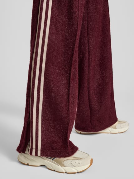 Vrouwenmodel draagt Sweatpants met elastische band van adidas Originals, los model, glittereffect, labelstitching, ritszakken, binnenbeenlengte maat S 81 cm, detailopname onderbenen.