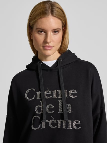 Vrouwenmodel draagt Oversized Hoodie met Kapuze van miss goodlife in zwart van puur katoen met labeldetail, tunnelkoord, ribboorden, Nahaufnahme Oberkörper.