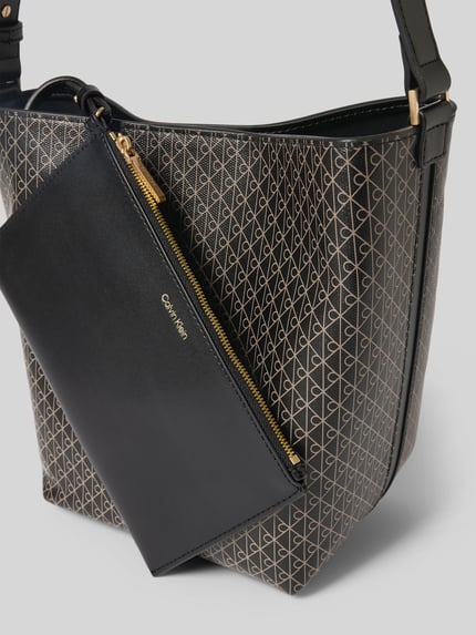 Produktfoto, Bucket Bag in Leder-Optik von CK Calvin Klein mit Allover-Logo-Print, Magnetverschluss, verstellbarem Schulterriemen, herausnehmbarer Innentasche mit Reißverschluss, Logo-Prägung, Hauptfach, Maße: Breite 27 cm, Länge 25 cm, Tiefe 12 cm, Länge Schulterriemen 50 cm, glatte und strukturierte Oberfläche in Schwarz und Gold.