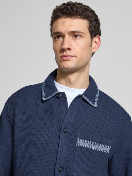 Männermodel trägt Relaxed Hemdjacke mit Strukturmuster von Scotch & Soda in Dunkelblau, reine Baumwolle, Nahaufnahme Oberkörper.