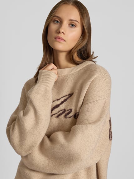 Frauenmodel trägt Oversized Strickpullover mit Label-Details von ANOTHER COTTON LAB in Beige, grobe Stricktextur, Nahaufnahme Oberkörper.