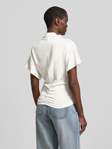 Frauenmodel trägt T-Shirt mit kurzem Stehkragen Modell 'Nupti' von My Essential Wardrobe, cremefarben, glatte Textur, Ganzkörperansicht Rückansicht. Viskose-Mix mit Stretch, körpernaher Schnitt, Rückenlänge bei Größe S 67 cm.