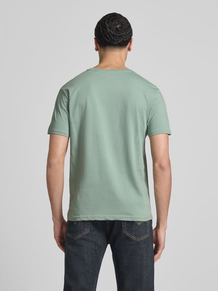 Männermodel trägt T-Shirt mit Label-Details Modell 'BASIC' von Alpha Industries in Grün, Reine Baumwolle, Gerader-Schnitt, Rückenlänge 67 cm, Ganzkörperansicht Rückansicht.