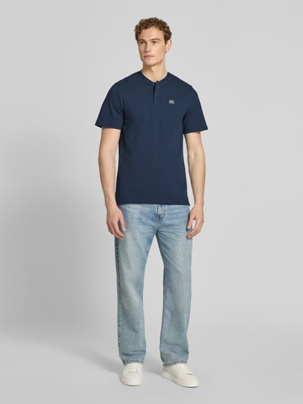 Mannelijk model draagt Regular Fit Poloshirt aus Baumwoll-Mix van s.Oliver RED LABEL in effen donkerblauw katoenmix piqué, label patch op de borst, henley-halslijn, korte mouwen, twee knopen; volledige lichaamsweergave van voren.