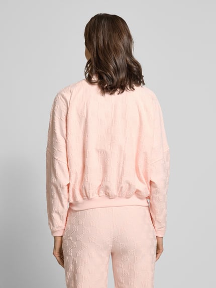 Frauenmodel trägt Oversized Sweatjacke aus Baumwoll-Mix Modell 'TERRYMONOGRAM_JACKET' von HUGO in Optik: Unifarben, Passform: Oversized, Verschluss: Reißverschluss, Muster: Allover-Muster, Applikation: Label-Stitching und Label-Prägung, Kragenform: Stehkragen, Ärmelform: Fledermausärmel, Ärmelabschluss und Rumpfabschluss elastisch, Material: Baumwoll-Mix, Ganzkörperansicht Rückansicht.