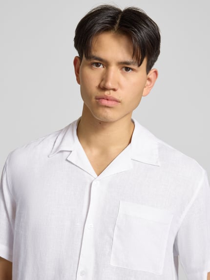 Männermodel trägt weißes Relaxed Fit Freizeithemd aus Leinen-Viskose-Mix Modell 'LAURENCE' von Only & Sons, Optik: Unifarben, Passform: Relaxed-Fit, Hemdkragen: Reverskragen, Knopfleiste: Einreihig, Ärmelform: Kurzarm, Brusttasche, Nahaufnahme Oberkörper.