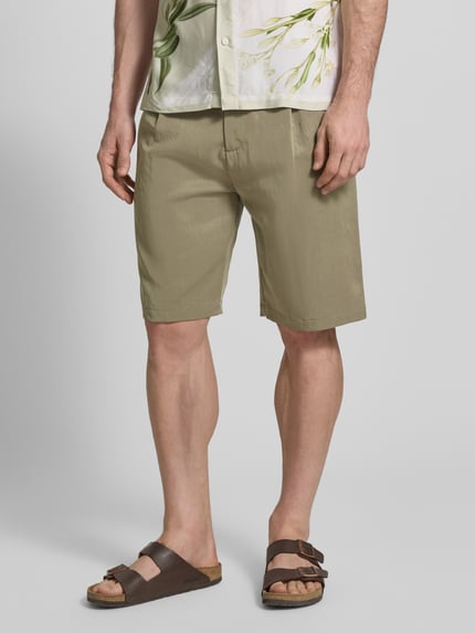 Mężczyzna nosi Regular Fit Shorts mit Gesäßtaschen Modell 'TAYLOR' od Guess, lyocell-mix, krój regular fit, kieszonki z tyłu, piaskowe, szerokość w rozmiarze 32: 46 cm, długość wewnętrzna nogawki: 28 cm, zapięcie na guzik i zamek, Ganzkörperansicht z przodu