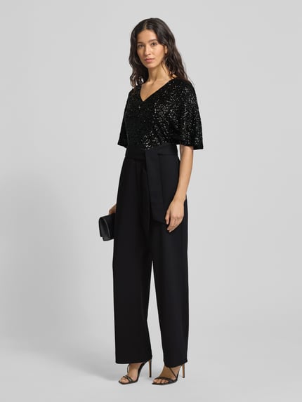 Frauenmodel trägt Taillierter Jumpsuit mit Paillettenbesatz von s.Oliver BLACK LABEL, Optik: Unifarben, Passform: Tailliert, V-Ausschnitt, Kappärmel, Reißverschluss, Label-Stitching, seitliche Eingrifftaschen, schwarze Farbe, schimmernde Struktur im Oberteil, fließendes Material, Ganzkörperansicht von vorne.