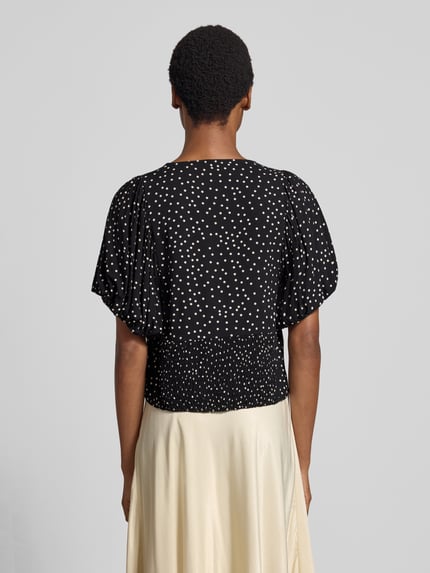 Vrouwenmodel draagt blouse met korte mouwen van zuiver viscose Model 'GILDA' van Soyaconcept, slim fit, v-hals, pofmouwen, ruglengte maat S 33 cm, mouwlengte maat S 27 cm, zwarte stof met witte stippen, gladde textuur, geheel van achteren