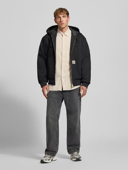 Männermodel trägt Regular Fit Freizeithemd aus reiner Baumwolle von G-Star RAW in Beige, kombiniert mit dunkler Jacke und Jeans, Ganzkörperansicht von vorne.