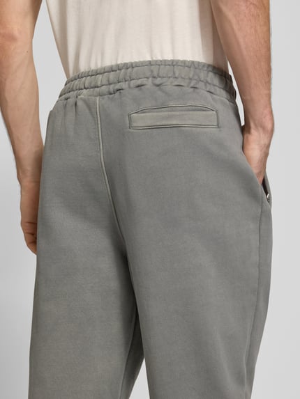 Männermodel trägt Loose Fit Sweatpants aus Baumwoll-Mix mit Label-Detail von PEGADOR in Grau mit elastischem Bund, Nahaufnahme Rückansicht.