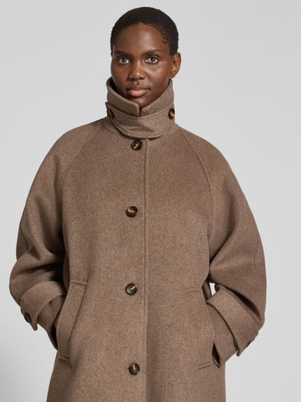Frauenmodel trägt Mantel aus Leinen-Mix mit Stehkragen Modell 'Keaton' von Neo Noir in Braun, strukturierte Oberfläche, Nahaufnahme Oberkörper.