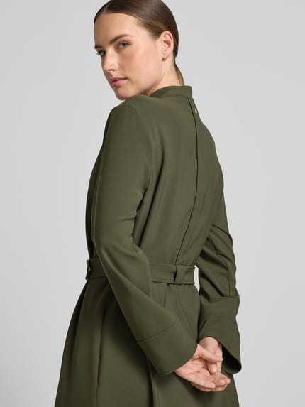 Frauenmodel trägt Knielanges Kleid mit Stehkragen und Gürtel von Marc Cain in Olivgrün, glatter Material-Mix mit Stretch-Anteil, Detailaufnahme Rückansicht, taillierter Schnitt, mittellange Ärmel.